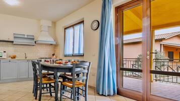 Un comedor con mesa y sillas, una cocina con armarios y estufa, y vista a un edificio a través de una ventana.