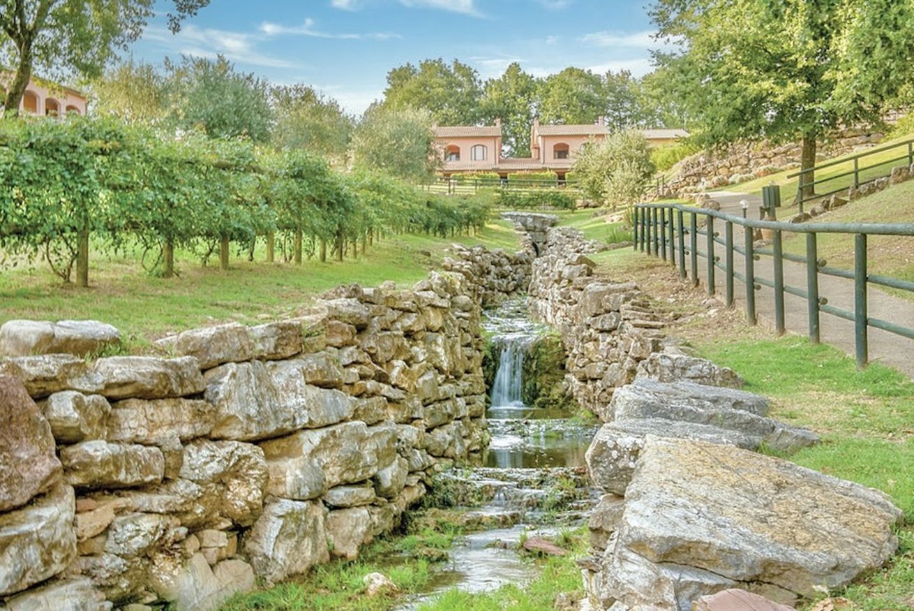 Ein von Steinmauern gesäumter Bach mit Wasserfall, umgeben von üppiger Vegetation und einer Steinmauer.