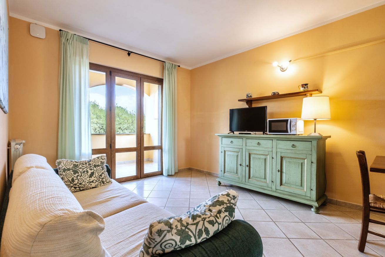 A room with a bed, a green cabinet with a television, and a window with curtains.