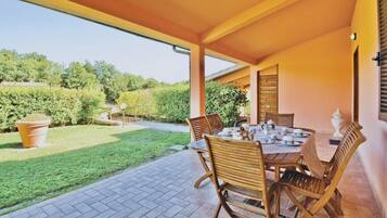 An outdoor patio with a table and chairs, surrounded by a garden and a view of the countryside.