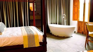 A four-poster bed with a striped blanket, a freestanding bathtub, and a round table in a hotel room. - Fishers House Hotel San Miguel (San Miguel de Allende)