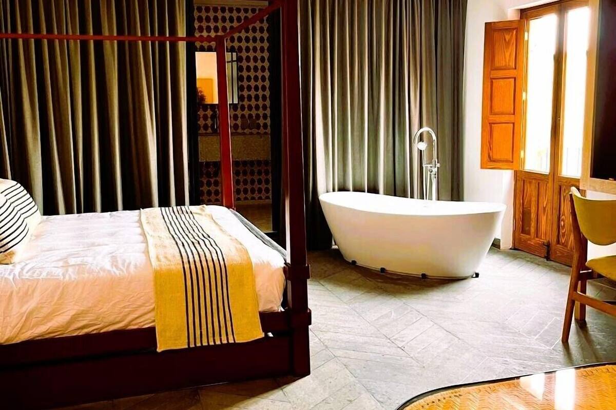 Un lit à baldaquin avec une couverture à rayures, une baignoire sur pieds et une table ronde dans une chambre d’hôtel.