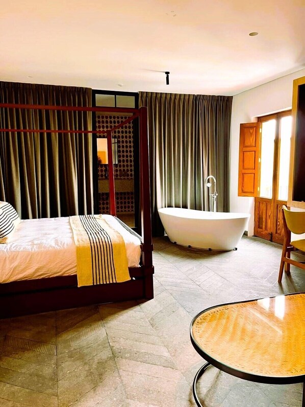 Una cama con dosel, una manta a rayas, una bañera independiente y una mesa redonda en una habitación de hotel.