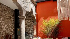An outdoor dining area with stone walls and red accents, featuring tables and chairs set for dining. - Fishers House Hotel San Miguel (San Miguel de Allende)