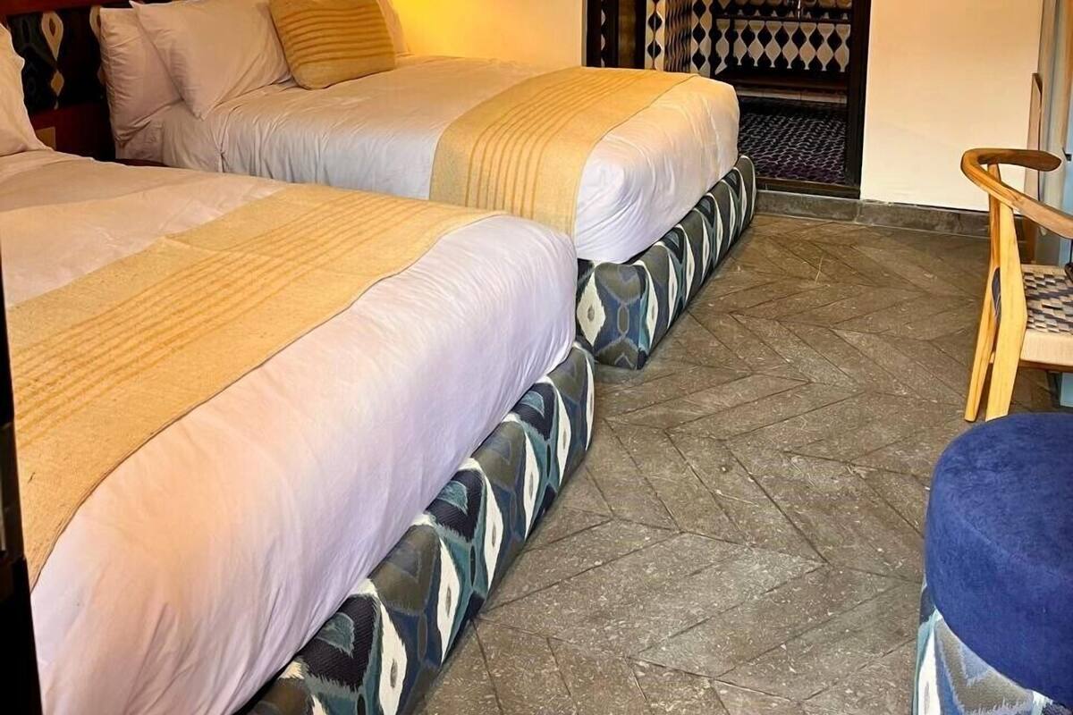 Une chambre d’hôtel avec deux lits, un petit coin salon et une salle de bain avec un mur décoré de motifs.