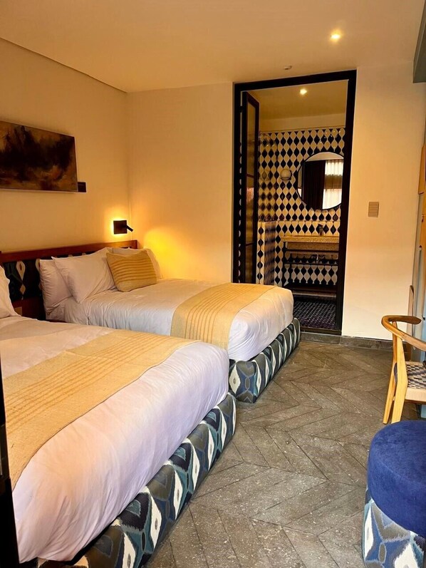 A hotel room with two beds, a small seating area, and a bathroom with a patterned wall.