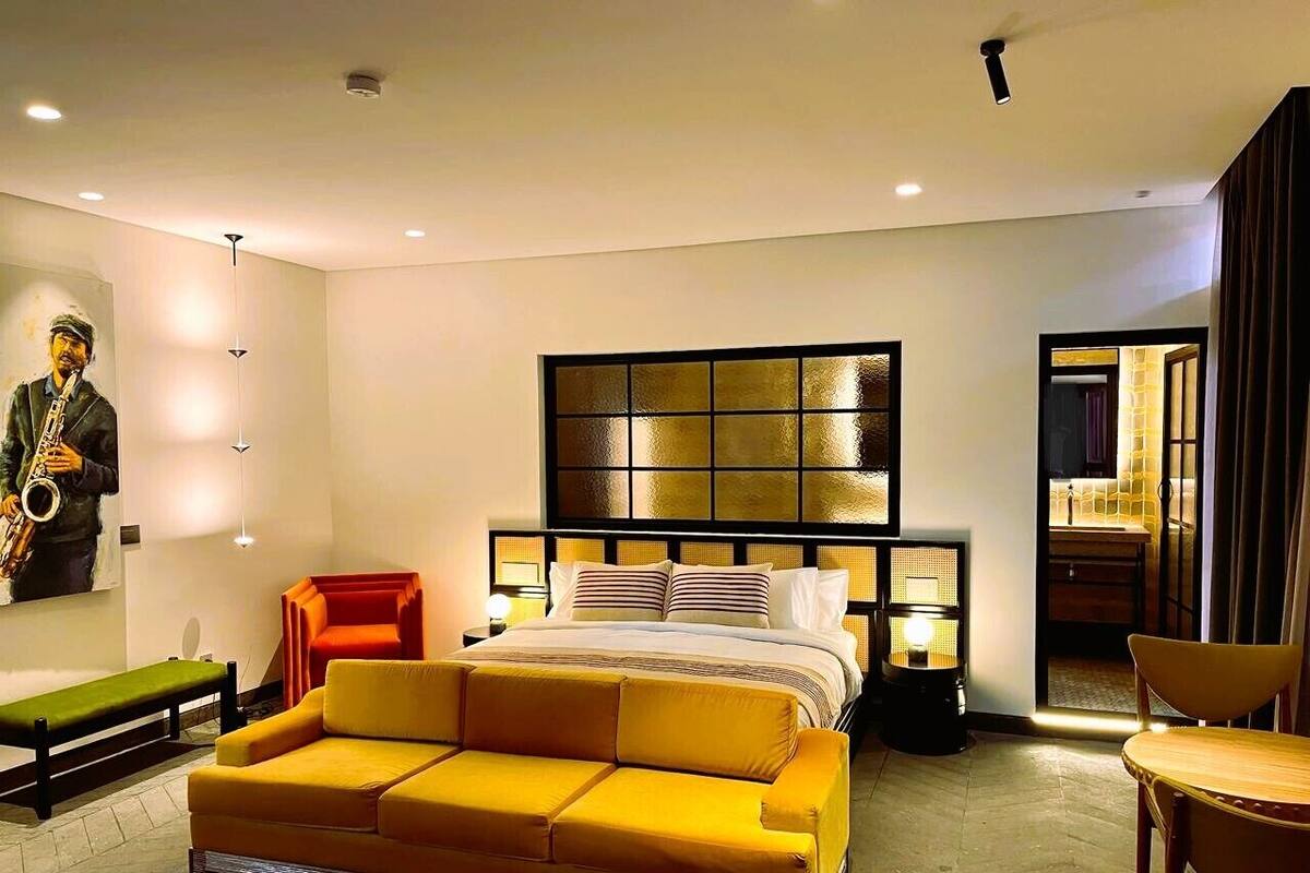 Une chambre d’hôtel moderne avec un grand lit, un canapé, un banc et une sculpture fixée au mur.