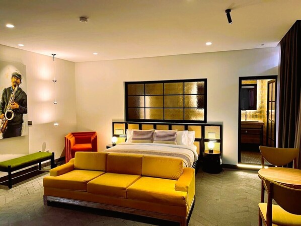 Quarto de hotel moderno com uma cama grande, um sofá, um banco e uma escultura na parede.