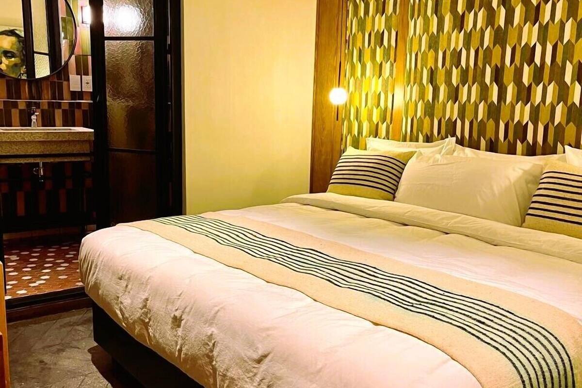 Une chambre d’hôtel avec un lit, une salle de bain avec un miroir et un mur décoré d’un motif.
