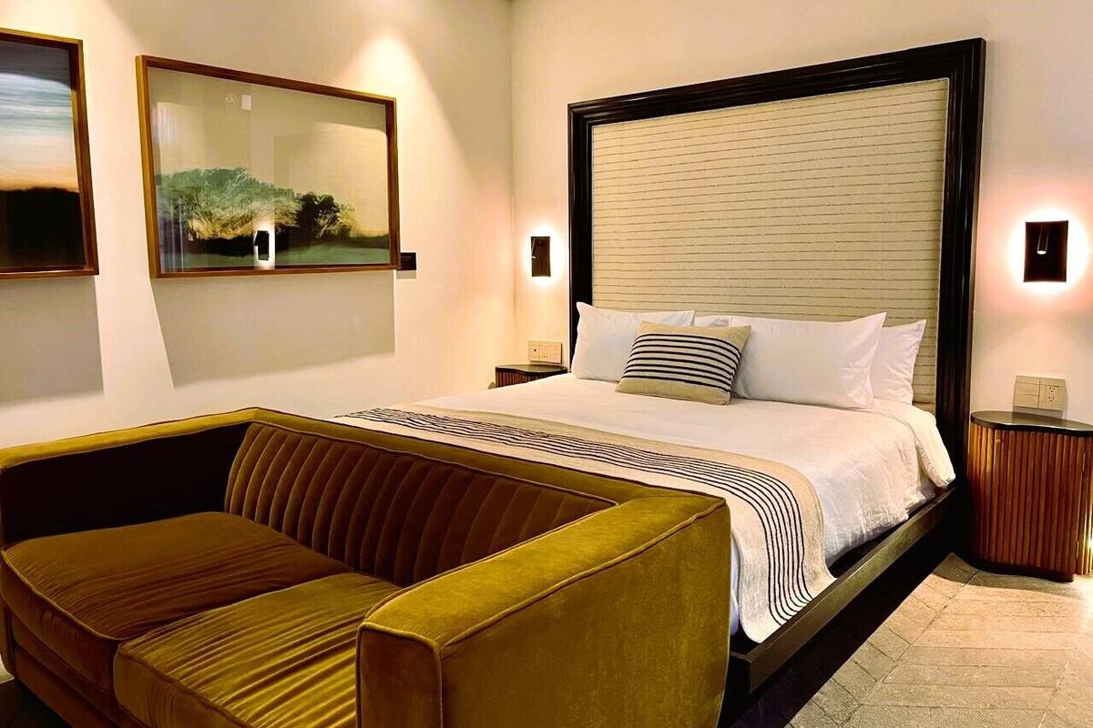 Une chambre d’hôtel moderne avec un grand lit, un canapé et deux lampes fixées au mur.