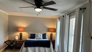 Ein Schlafzimmer mit einem Bett, zwei Nachttischlampen, einem Deckenventilator und einem Fenster mit Vorhängen.