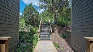 Una escalera de madera que conduce a un espacio cubierto rodeado de árboles y vegetación.