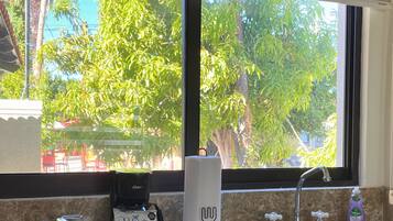 Una cocina con ventana, una cafetera, un dispensador de toallas de papel, un lavabo y una botella de detergente.