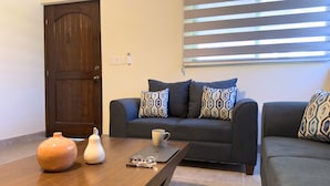 A living room with a dark wooden door, a sofa with patterned cushions, a coffee table with a vase, glasses, and a notebook. - Posada Don Esteban by PartnerHost (Loreto)