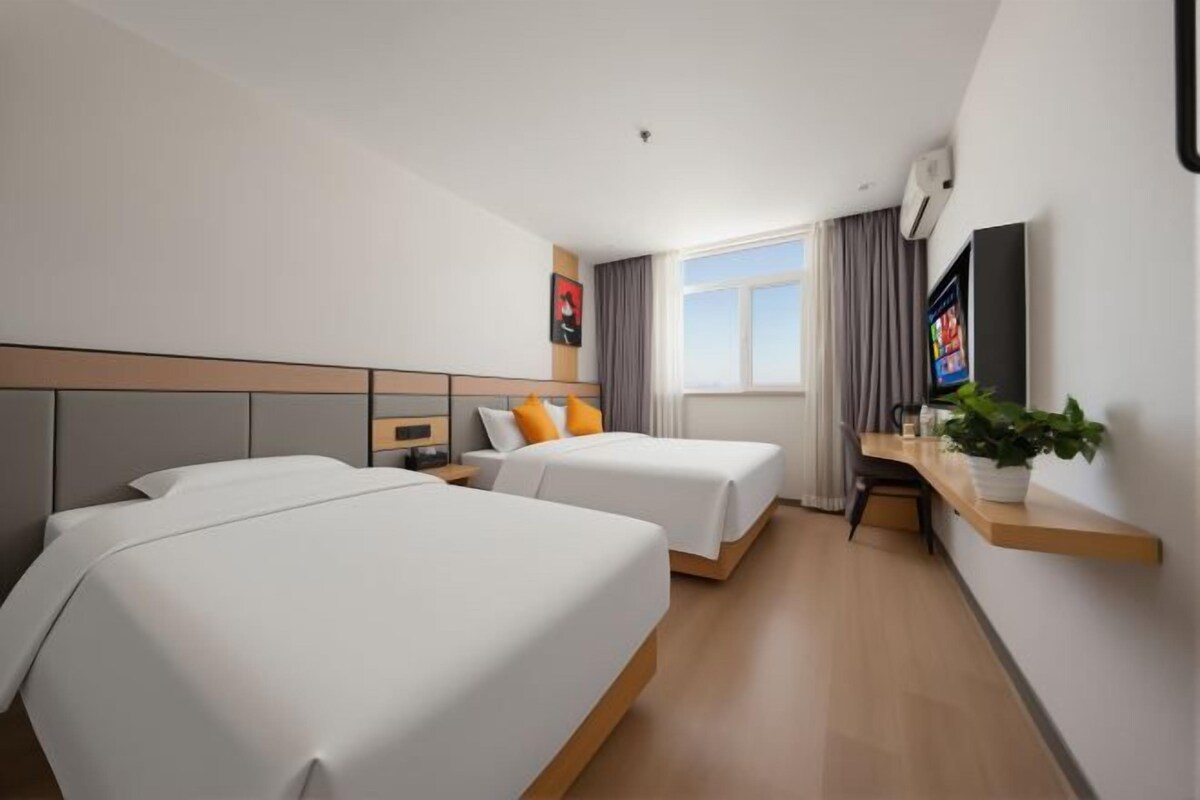 A hotel room with two beds, a desk, a TV, and a window with curtains.