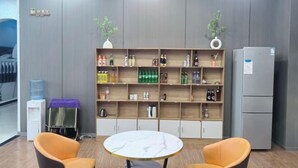 Una habitación con una mesa de mármol, dos sillas anaranjadas, una estantería con varios objetos y un refrigerador gris.
