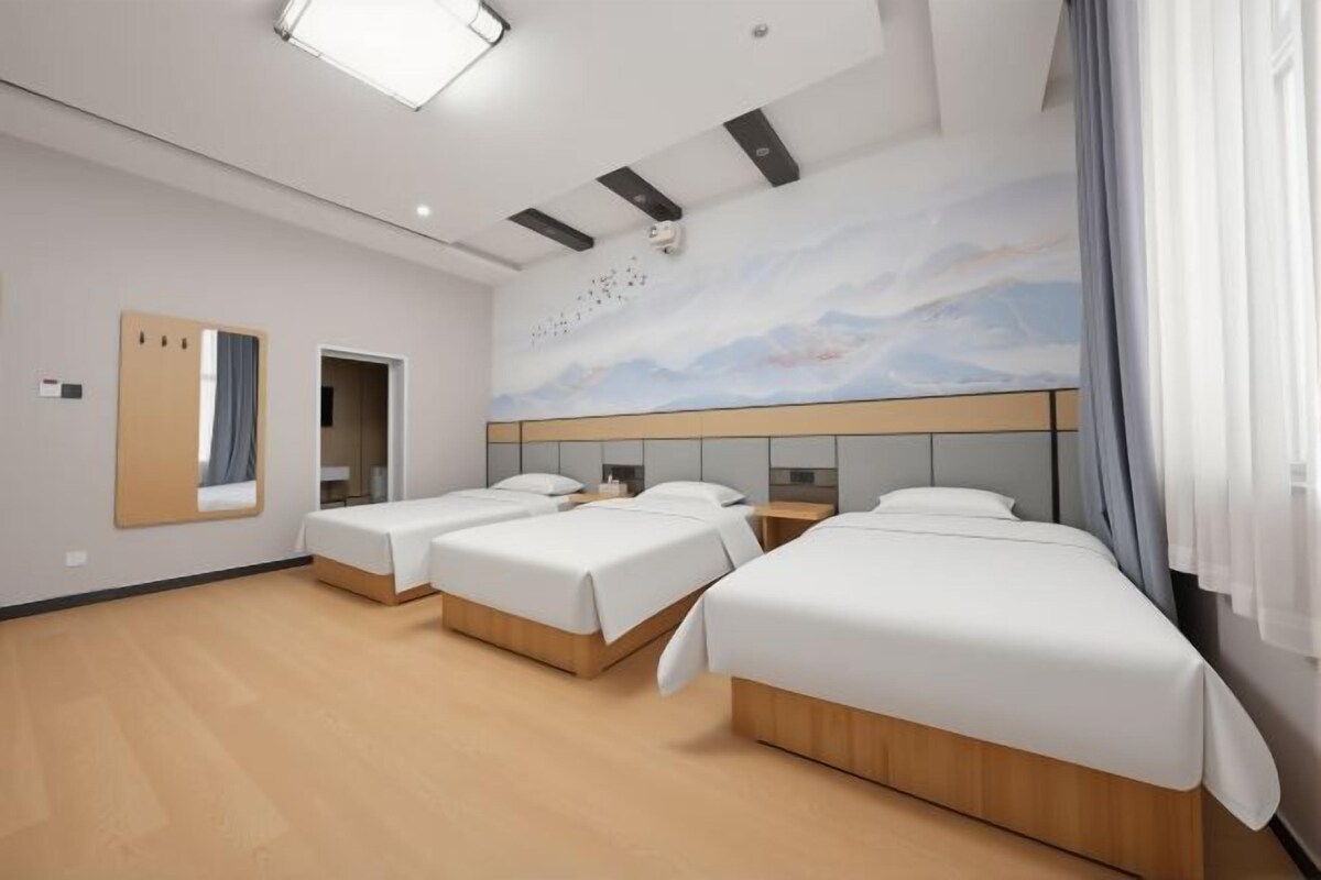 A hotel room with three beds, a large mirror, a painting on the wall, and a wooden floor.
