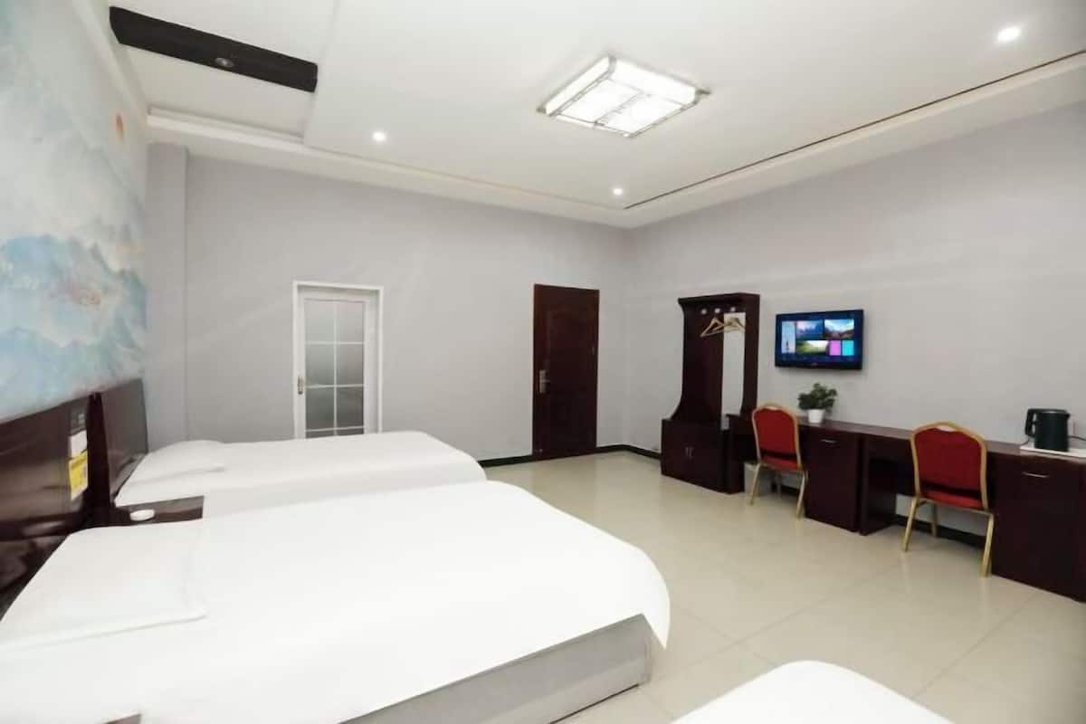 Una habitación de hotel con dos camas, un escritorio con sillas, un televisor y una puerta.