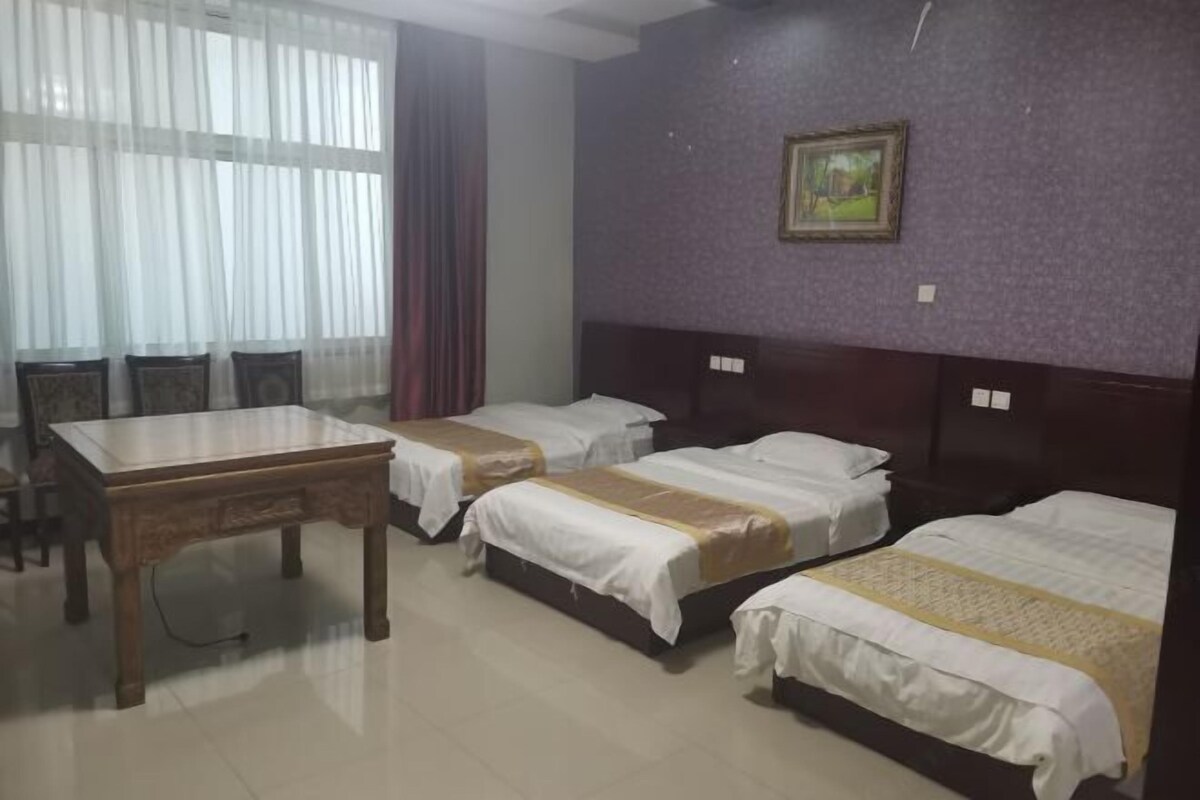 A hotel room with two single beds, a wooden table, and a window with sheer curtains.