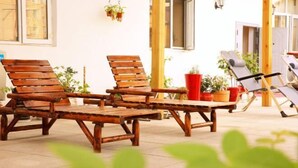 Un espace extérieur aménagé avec des meubles de jardin en bois, comprenant des fauteuils et des tables, ainsi que des plantes en pot. Une porte est visible au fond.