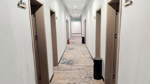 Un couloir d’hôtel avec des portes portant les numéros A12, une moquette à motifs et une poubelle.