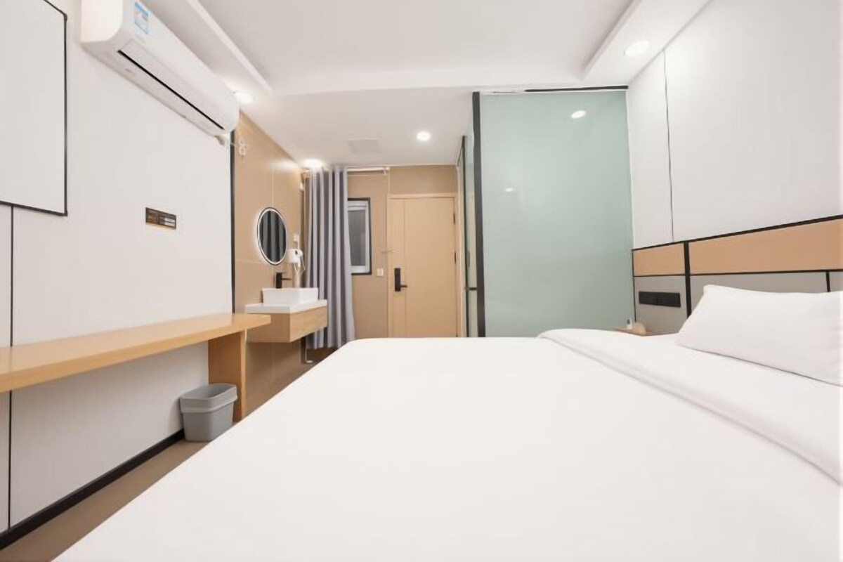 A hotel room with a bed, bedside table, mirror, and a small trash bin.