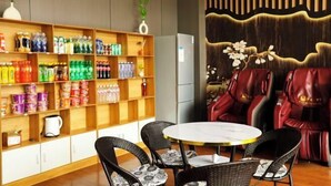 Une pièce comprenant une table ronde et quatre chaises, une bibliothèque remplie de divers objets, et un coin salon avec des fauteuils en cuir rouge.