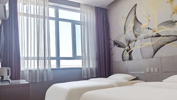 Une chambre d’hôtel avec deux lits, une grande fenêtre avec des rideaux légers, un climatiseur fixé au mur et un tableau représentant des formes abstraites.
