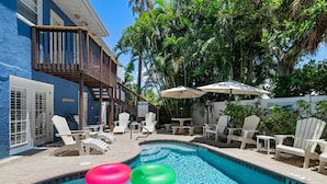 A pool area with a blue pool, white lounge chairs, and a wooden deck. - AMI Condo W/Pool, Walk to Beach, Bars, Restaurants and Fishing! (Bradenton Beach)