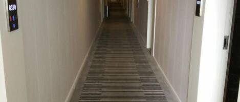 Un pasillo de hotel con suelo alfombrado, puertas a ambos lados y un letrero en la pared izquierda.