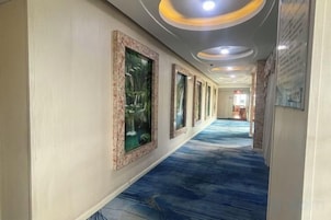 A hotel corridor with framed artwork on the walls, a blue carpet, and recessed lighting.