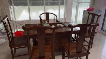 A dining area with a wooden table and chairs, a window with a view, and a red bucket on the floor.