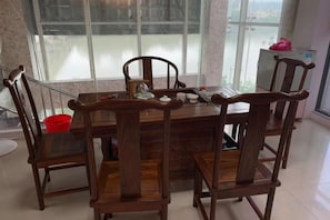 Un coin repas avec une table et des chaises en bois, une fenêtre donnant sur un beau paysage et un seau rouge posé sur le sol.