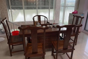 A dining area with a wooden table and chairs, a window with a view, and a red bucket on the floor.
