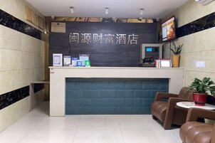 A reception desk with a digital screen, a cash register, and a small plant. There are leather chairs and a table with a red pot.