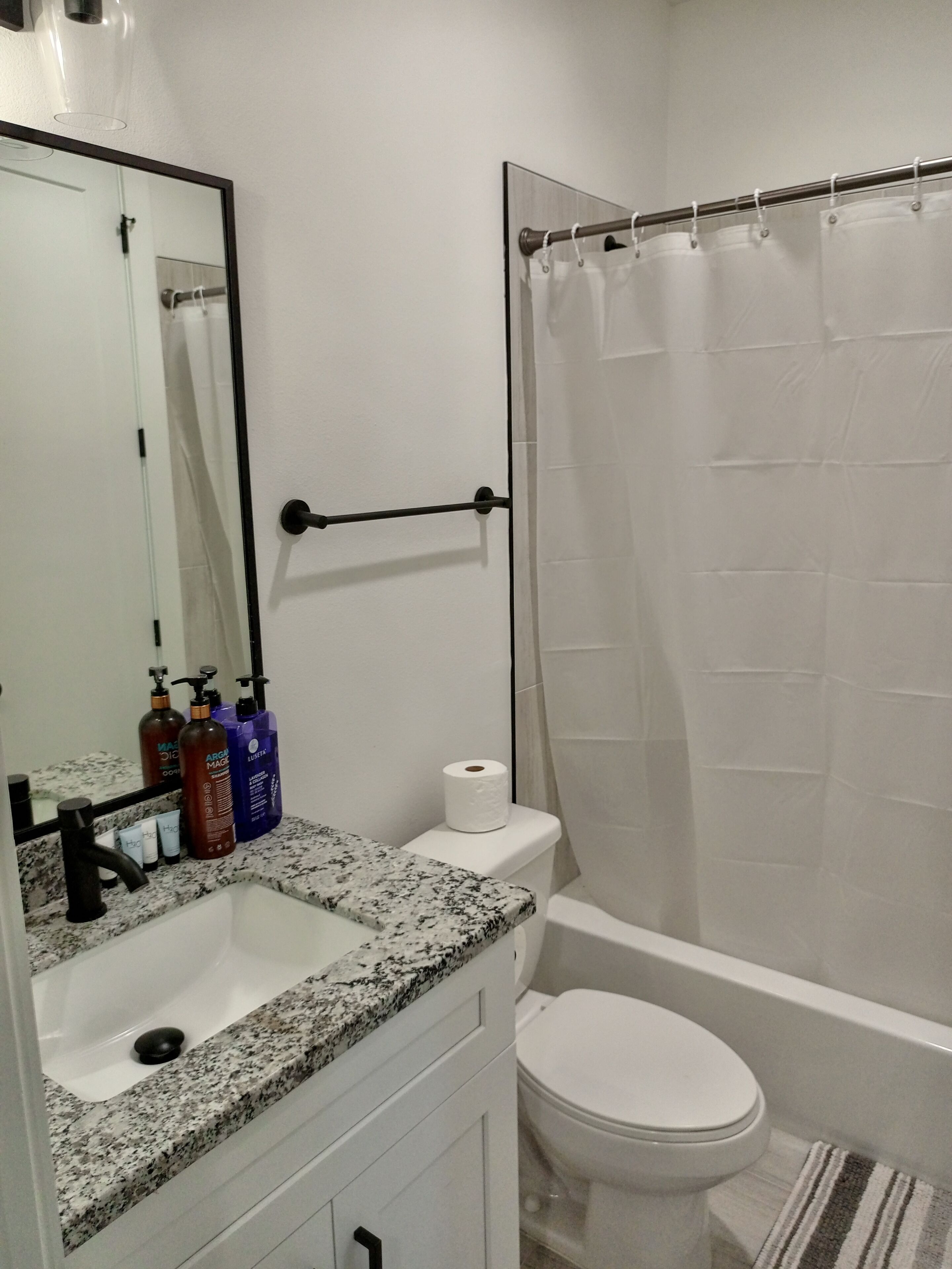 A bathroom with a sink, mirror, toilet, and shower curtain.