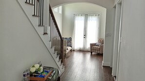 Un hall d’entrée spacieux avec un escalier en bois, une table en verre ornée de divers objets et une chaise à motifs.