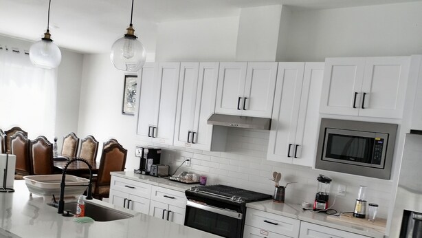 Une cuisine moderne avec des meubles blancs, un îlot central, un réfrigérateur en acier inoxydable et un four à micro-ondes.