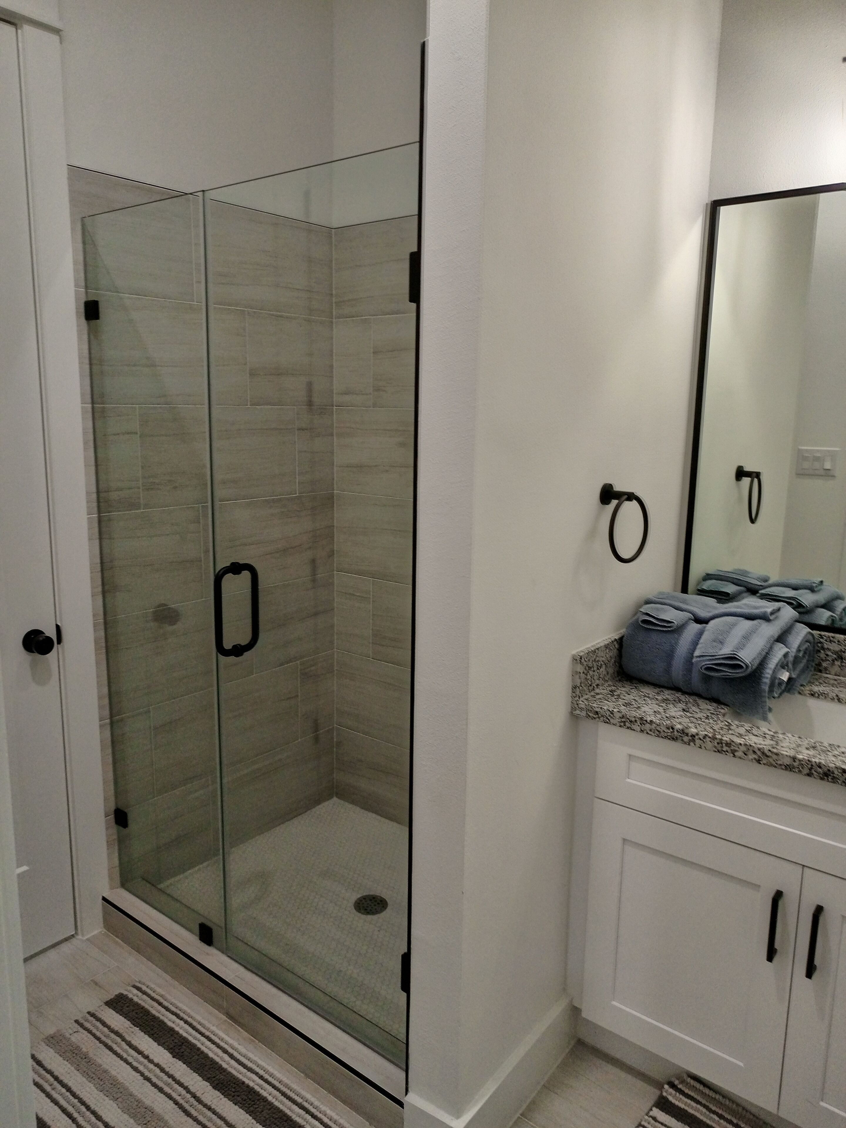 A modern bathroom with a glass-enclosed shower, white cabinets, and a granite countertop.