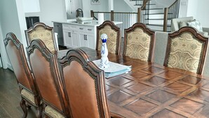 Une salle à manger avec une grande table en bois et des chaises décorées, une cuisine à l’arrière-plan et un escalier menant à l’étage supérieur.