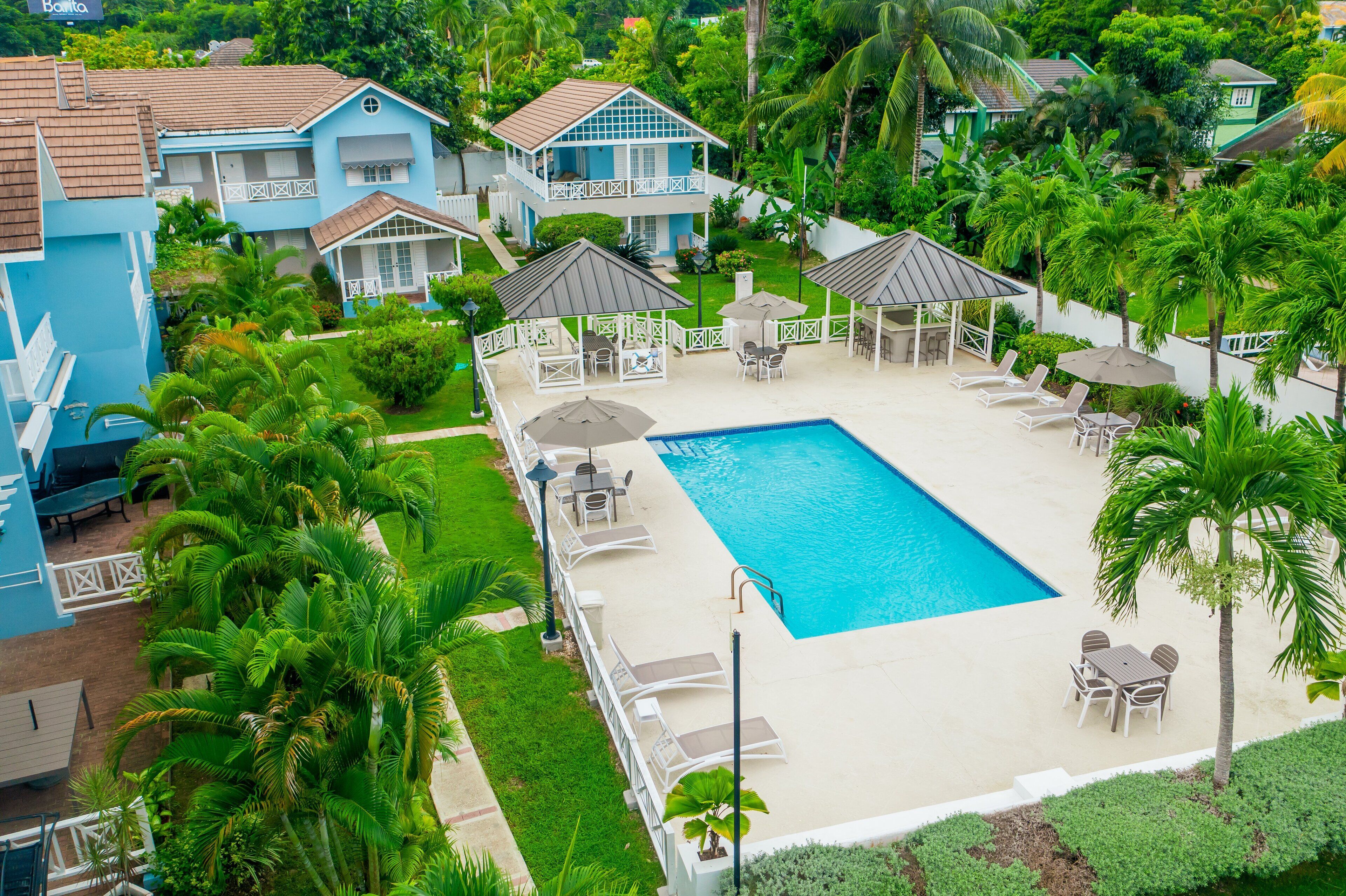 A resort with a swimming pool, lounge chairs, umbrellas, and a garden area.