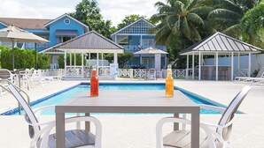 A poolside area with a table and chairs, two umbrellas, and a pool. - 🏝️ Sleep to Caribbean Waves Pool | Beach + Pool + AC • Ocho Rio (Ocho Rios)