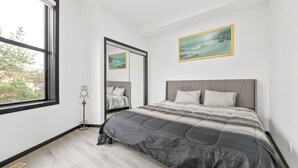 Um quarto com uma cama grande, uma janela, um espelho e um quadro na parede.