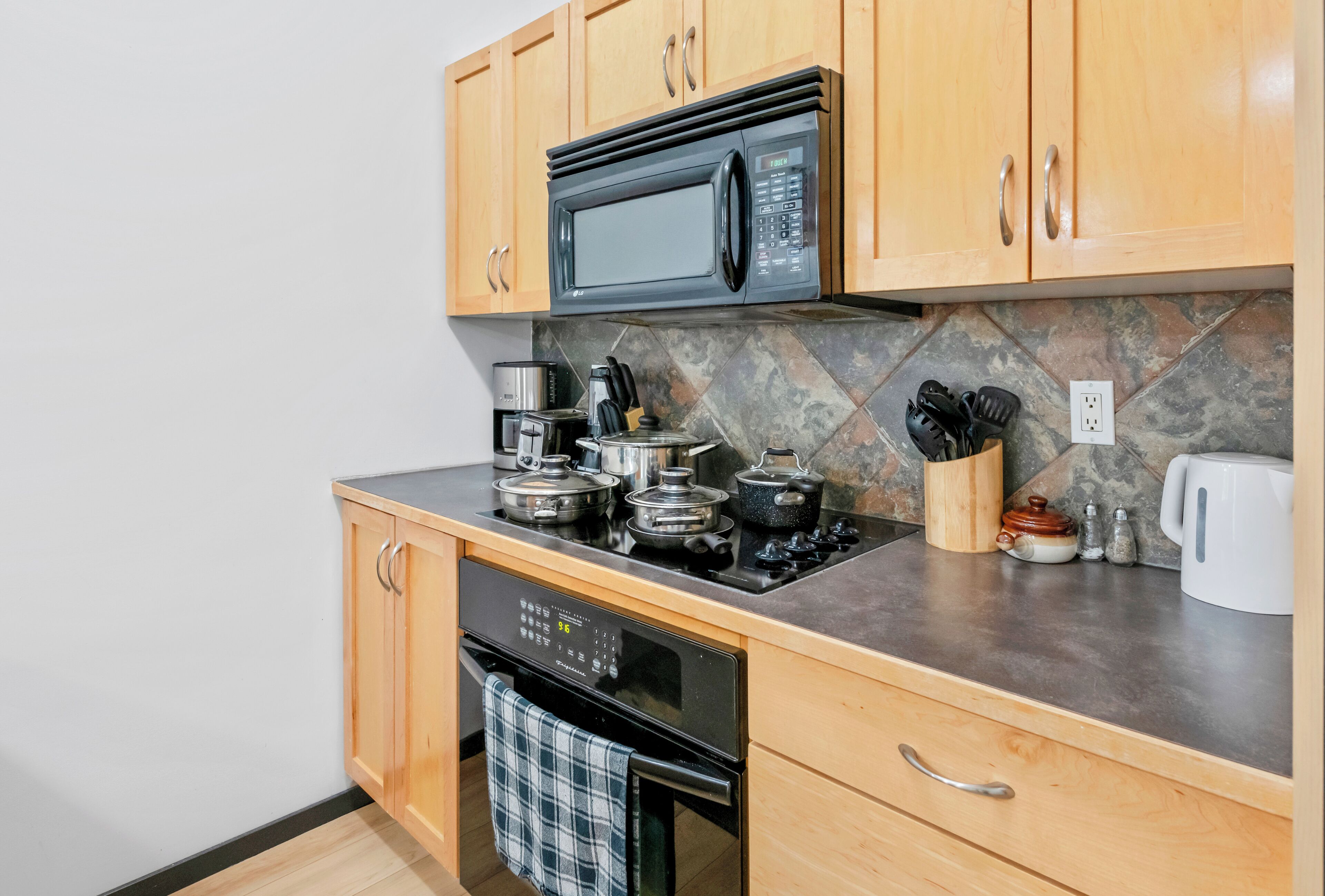 A compact kitchen with wooden cabinets, a built-in microwave, a stove, and a dishwasher.