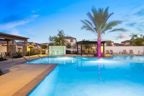 A swimming pool with a palm tree, lounge chairs, and a covered area with a pergola.