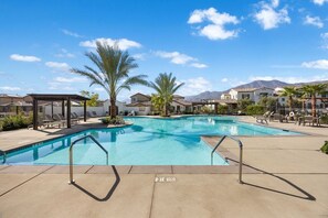Una piscina con sillas de descanso y palmeras, rodeada de edificios y montañas.