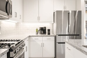 A modern kitchen with white cabinets, stainless steel appliances, and a granite countertop.