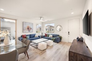A modern living room with a glass coffee table, sofas, and a flat-screen TV.