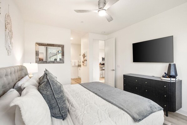 A bedroom with a bed, a dresser, a television, and a ceiling fan.