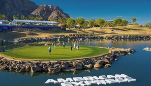 A golf course with a water body, a mountain in the background, and a large sign reading 'AMERICAN EXPRESS'.